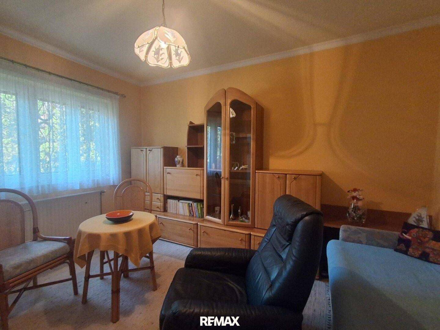Wohnzimmer mit Holzmöbeln, gelben Wänden und einem Fenster mit Blick ins Grüne.