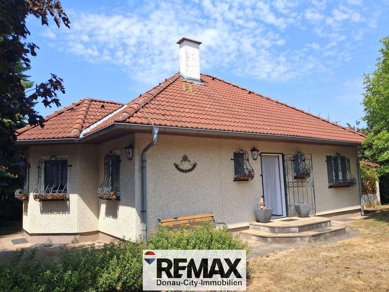 Rückansicht des Hauses mit Terrasse, rotem Ziegeldach und Garten.