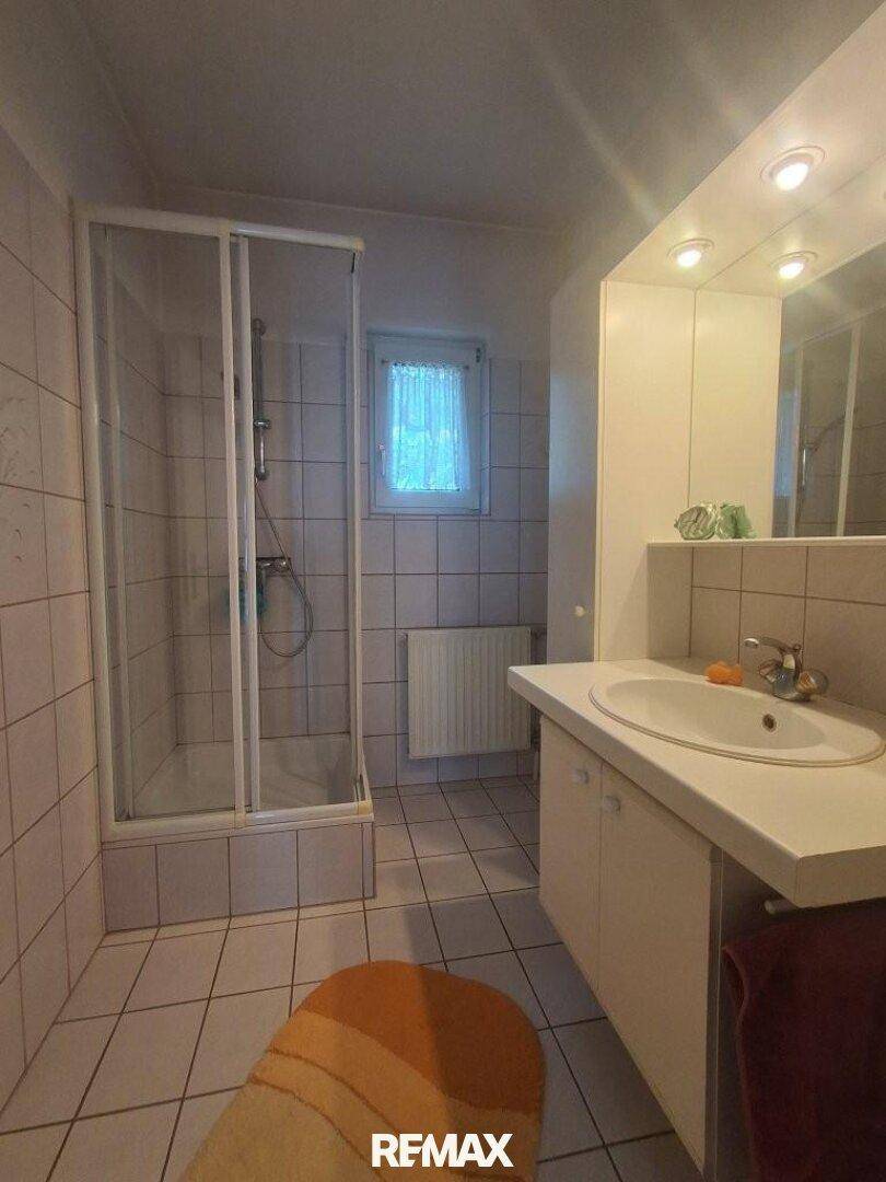 Badezimmer mit Duschkabine, Waschbecken und weißen Fliesen.