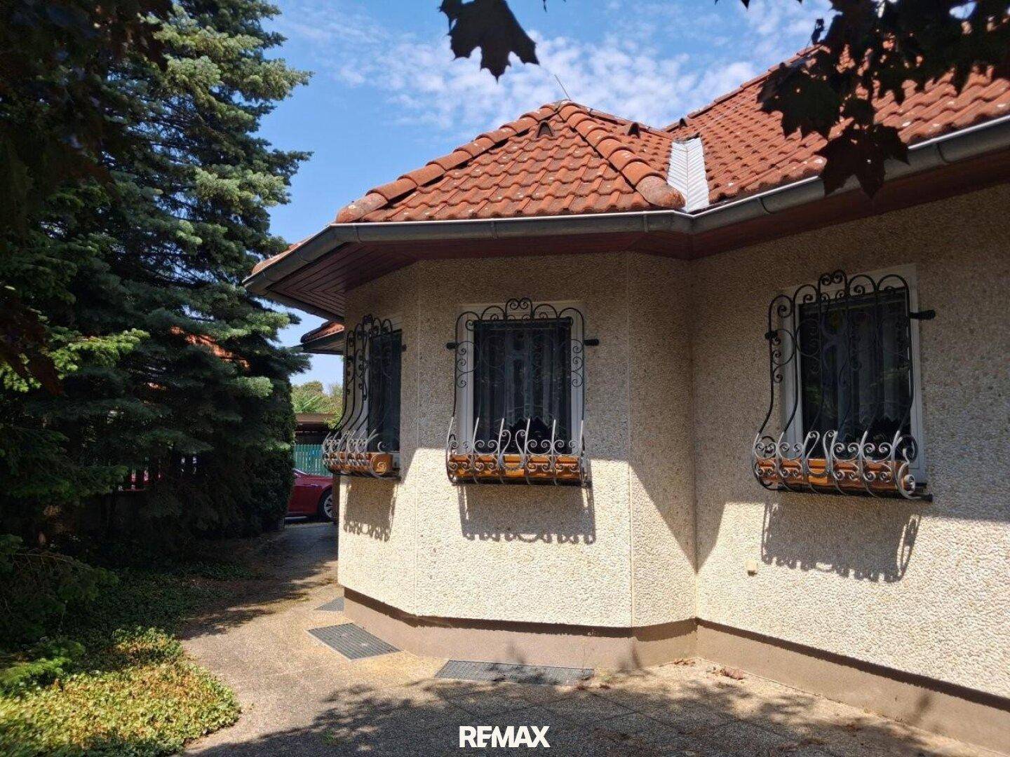 Eckansicht des Hauses mit dekorativen Fenstergittern und einem roten Ziegeldach.