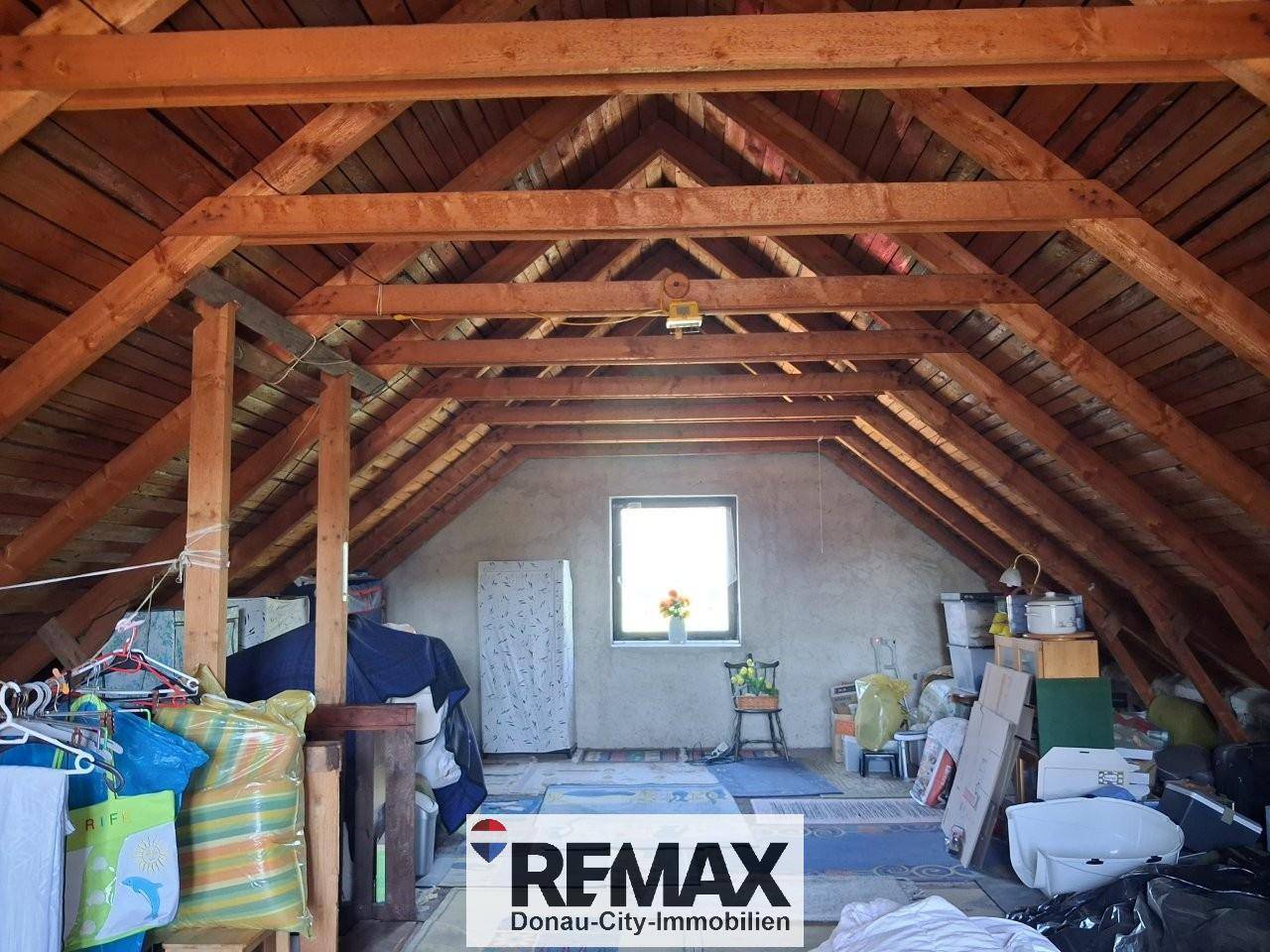 Geräumiger Dachboden mit sichtbaren Holzbalken und Fenster, bietet Stauraum.
