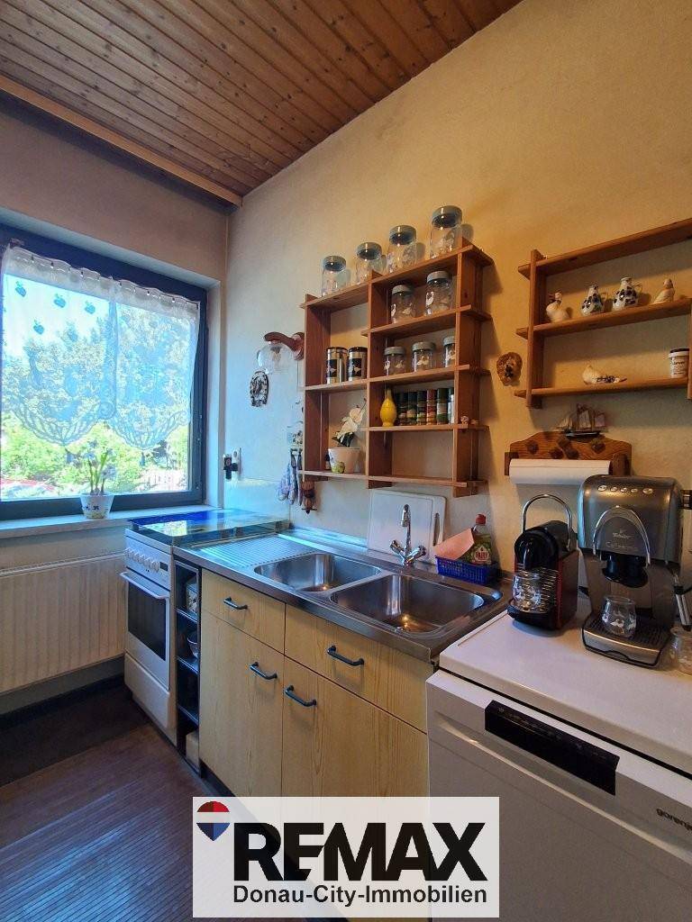 Funktionale Küche mit Holzregalen, Doppelspüle und Fenster mit Blick nach draußen.
