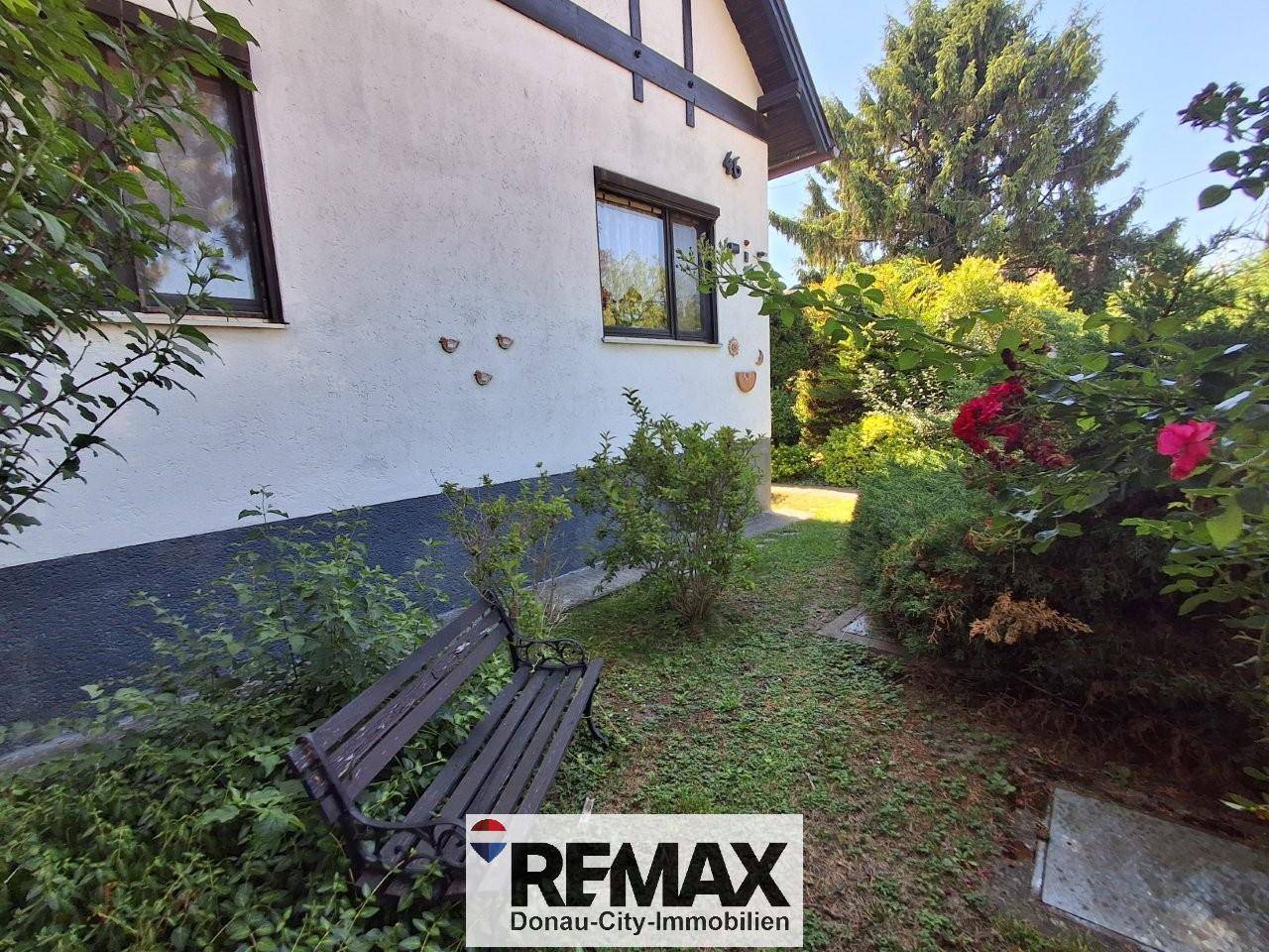 Ruhiger Gartenbereich neben dem Haus mit einer Holzbank und blühenden Rosen.