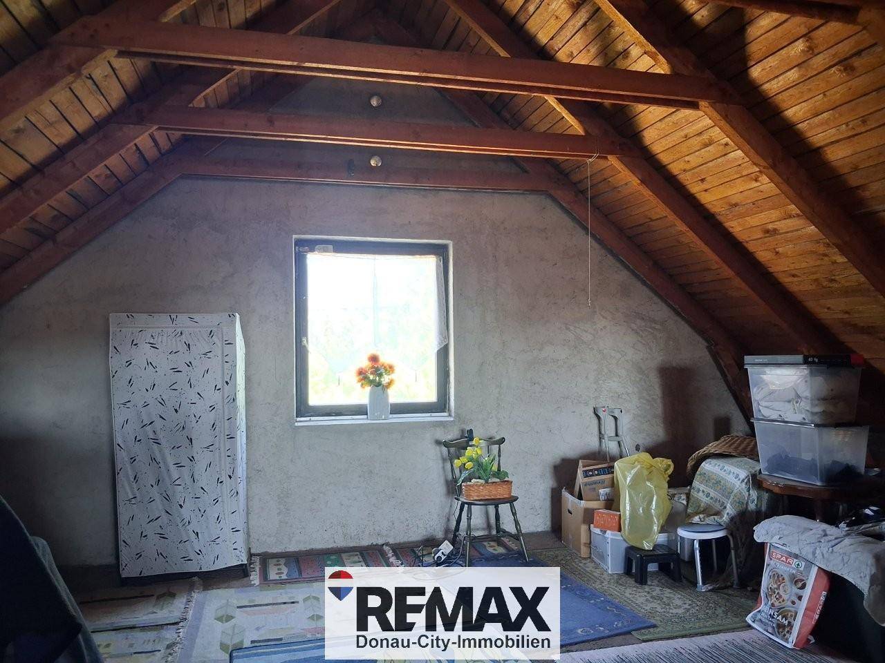 Geräumiger Dachboden mit sichtbaren Holzbalken und Fenster, bietet Stauraum.