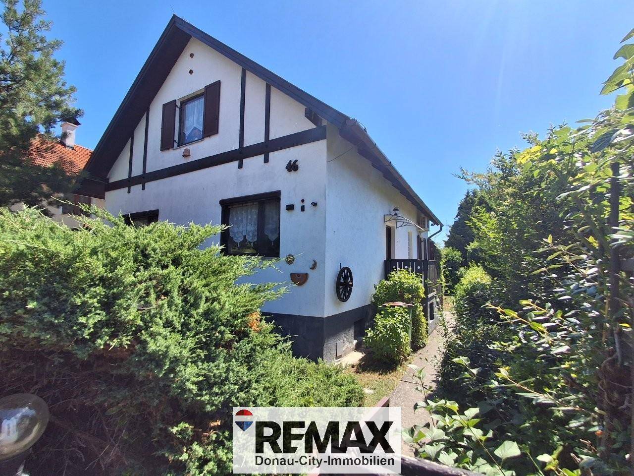 Ansicht des Hauses von der Seite mit weißer Fassade, dunklen Holzelementen und dichten Hecken.