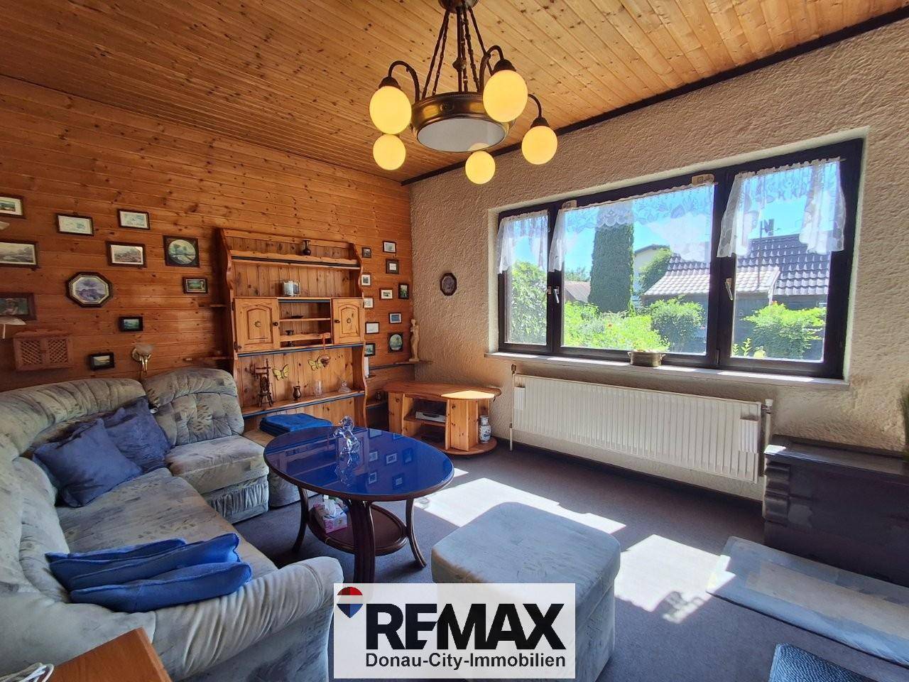 Geräumiges Wohnzimmer mit bequemer Couch, Holzdecke und Blick ins Grüne.