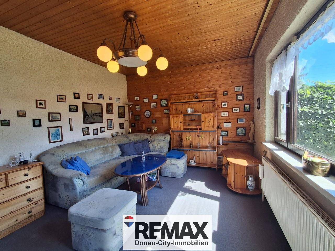 Geräumiges Wohnzimmer mit bequemer Couch, Holzdecke und Blick ins Grüne.