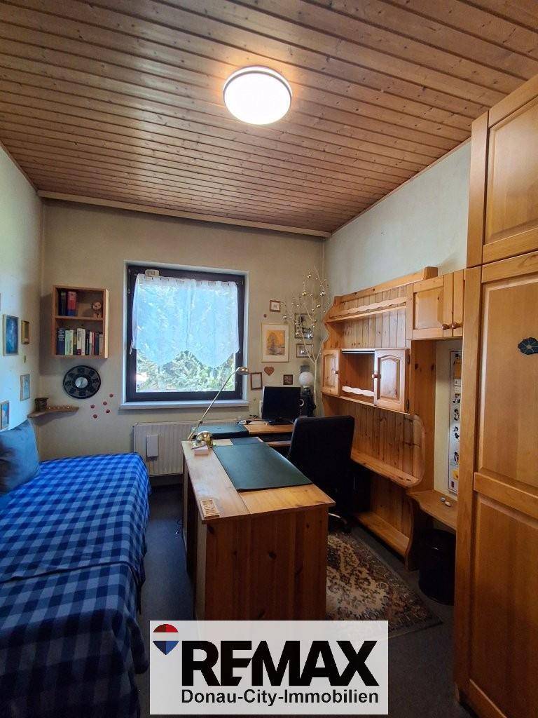 Helles Schlafzimmer mit Holzdecke, Schreibtisch und Blick ins Grüne.