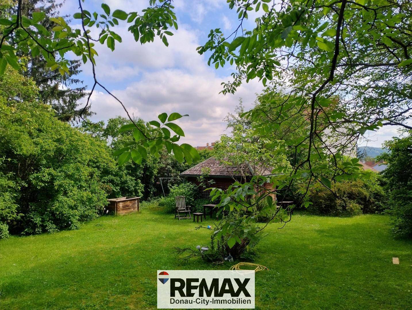 Weitläufiger Gartenbereich mit einer kleinen Holzhütte und Sitzgelegenheiten unter Bäumen.
