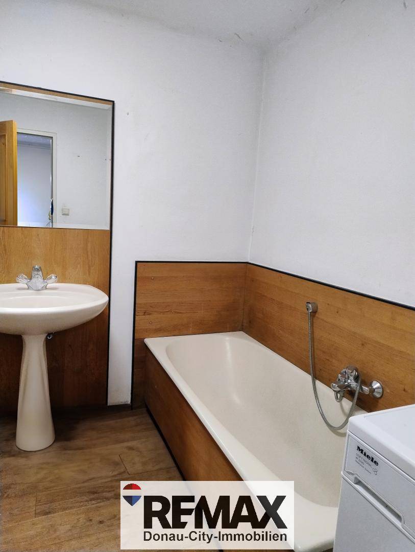 Badezimmer mit Badewanne, Waschbecken und Waschmaschine, teilweise mit Holzverkleidung an den Wänden.