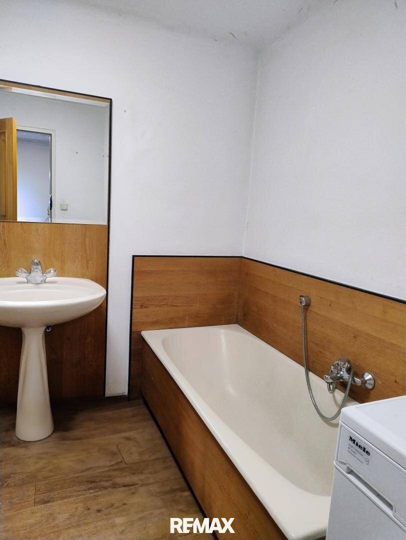Badezimmer mit Waschbecken, Badewanne und Holzverkleidung an den Wänden.