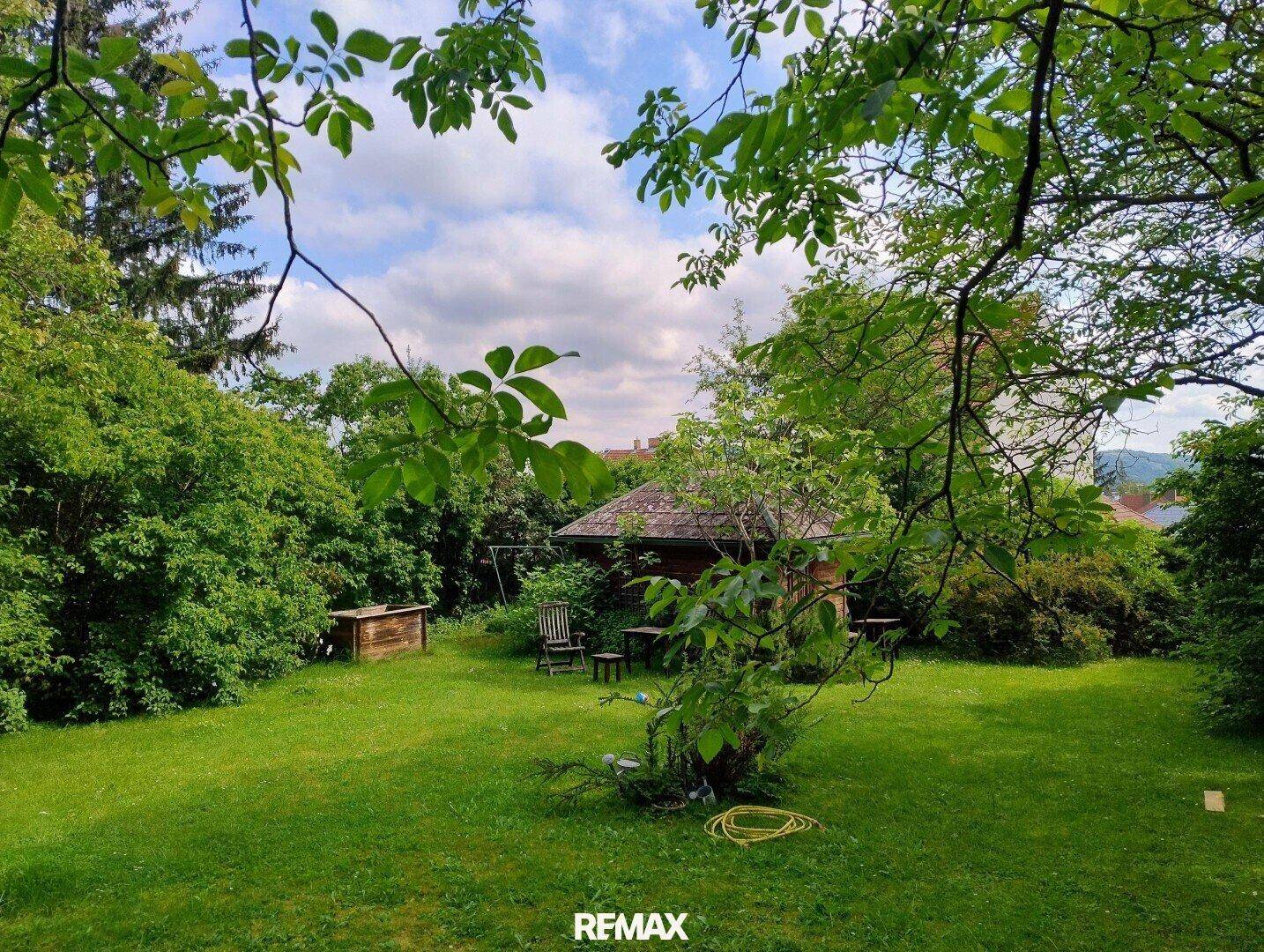 Großer, gepflegter Garten mit Rasenfläche, Bäumen und einem kleinen Gartenhaus im Hintergrund.