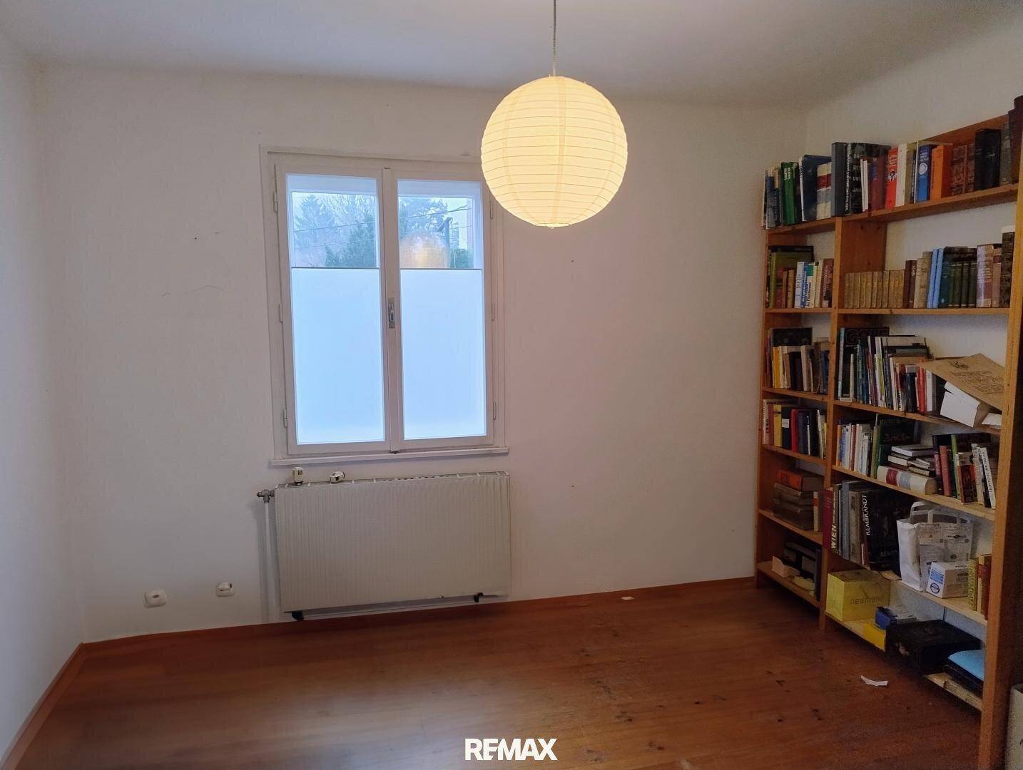 Helles Zimmer mit Holzboden, großem Fenster und Bücherregal, ideal als Schlaf- oder Arbeitszimmer.