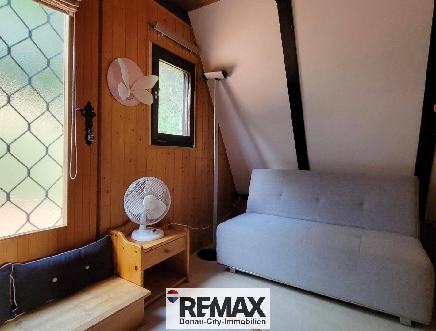 Gemütlicher kleiner Raum mit Holzwänden, Sofa und Fenster, ideal als Rückzugsort.