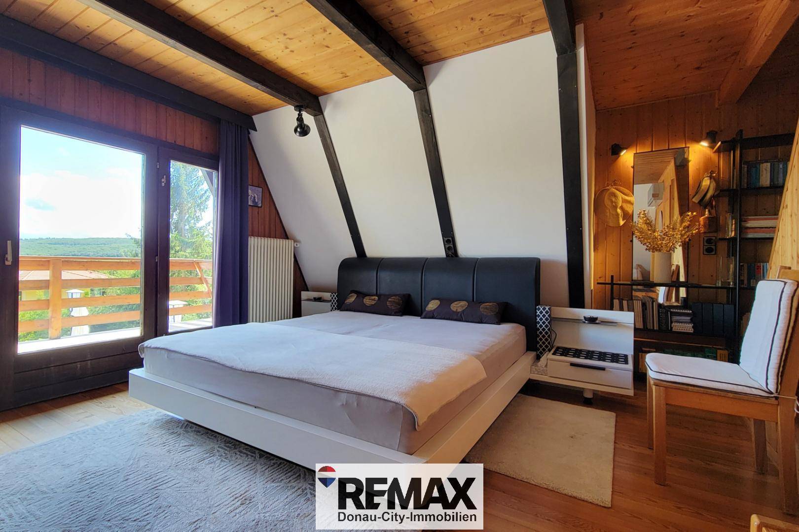 Schlafzimmer mit Holzwänden, Dachschräge, Doppelbett und Balkonzugang mit Fernblick.