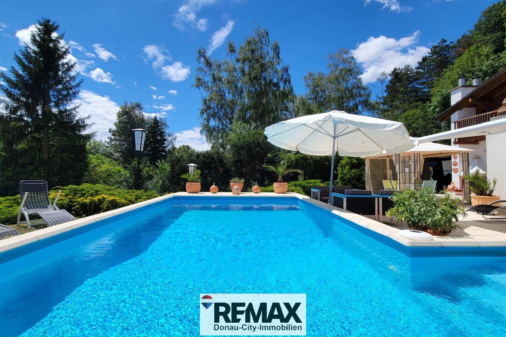 Großzügiger Poolbereich mit blauer Wasseroberfläche, Sonnenschirm und angrenzender Terrasse.
