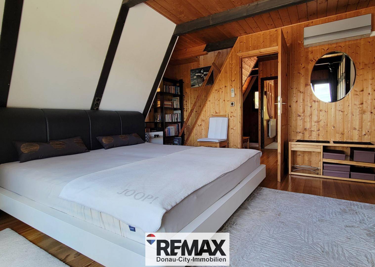 Rustikales Schlafzimmer mit Holzwänden, Dachschräge und Zugang zu einem weiteren Raum.