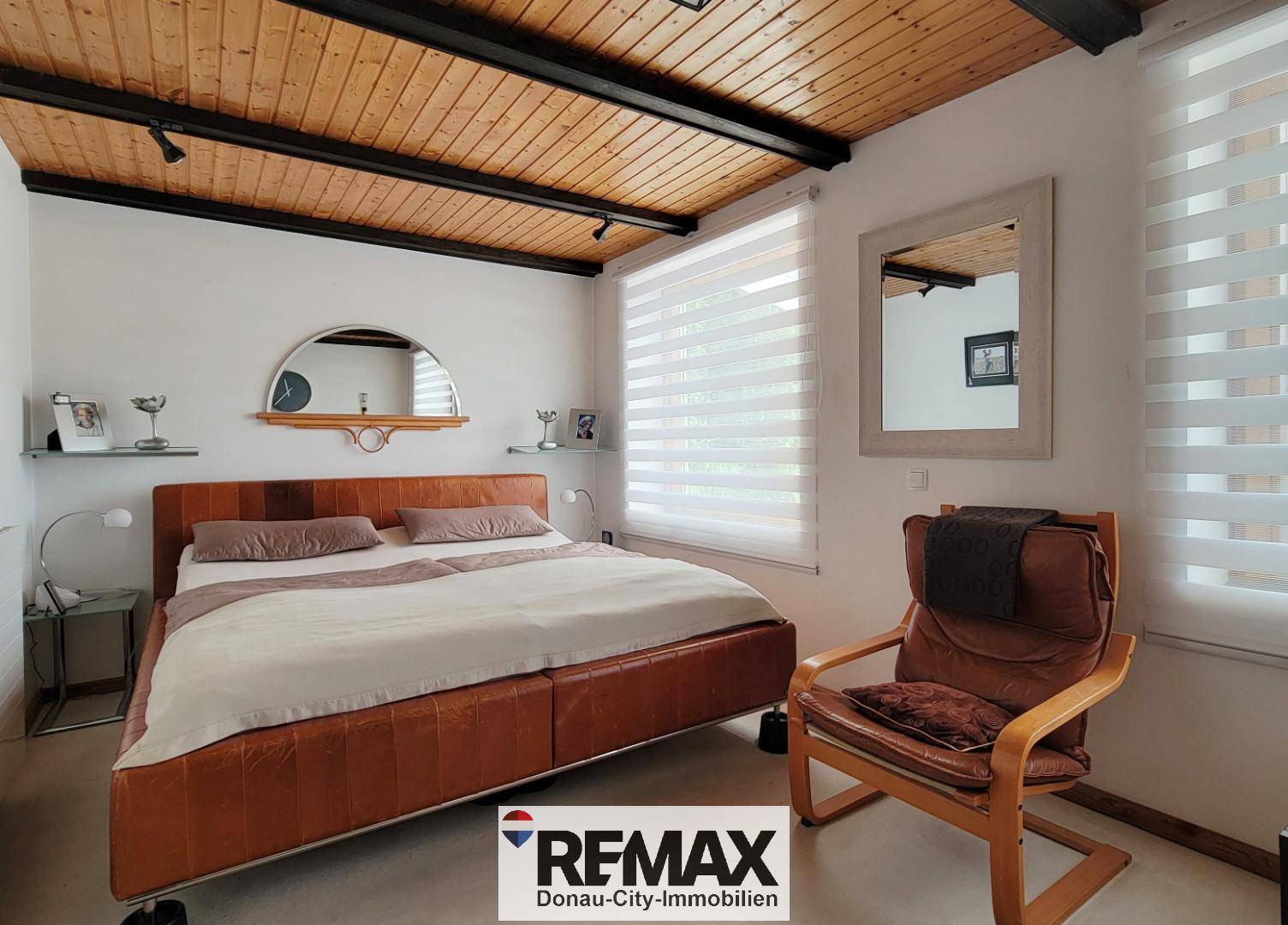 Gemütliches Schlafzimmer mit Holzbalkendecke, Doppelbett und Fenster mit Jalousien.