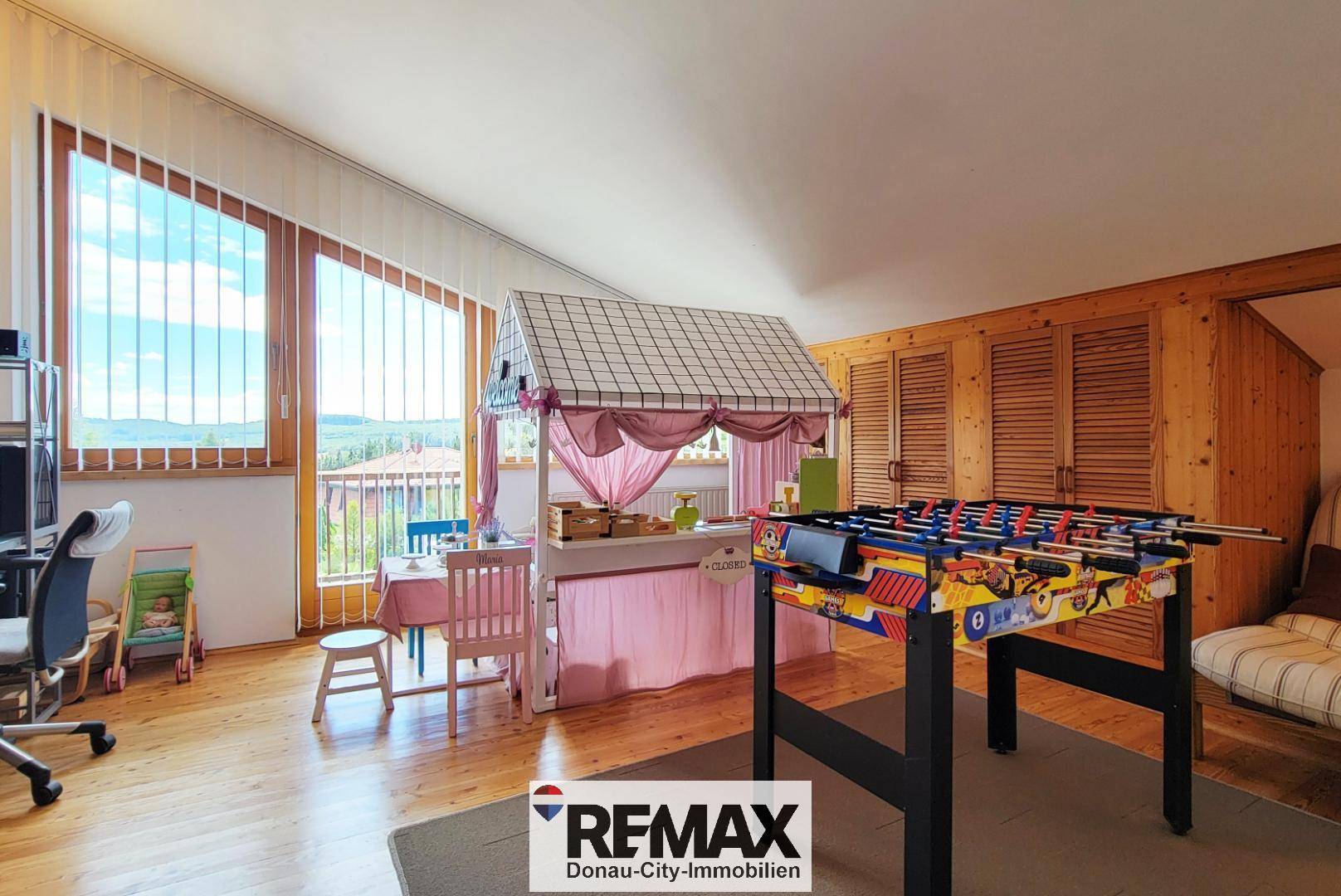 Helles Spielzimmer mit Holzboden, großen Fenstern, Tischfußball und Kinderbereich.