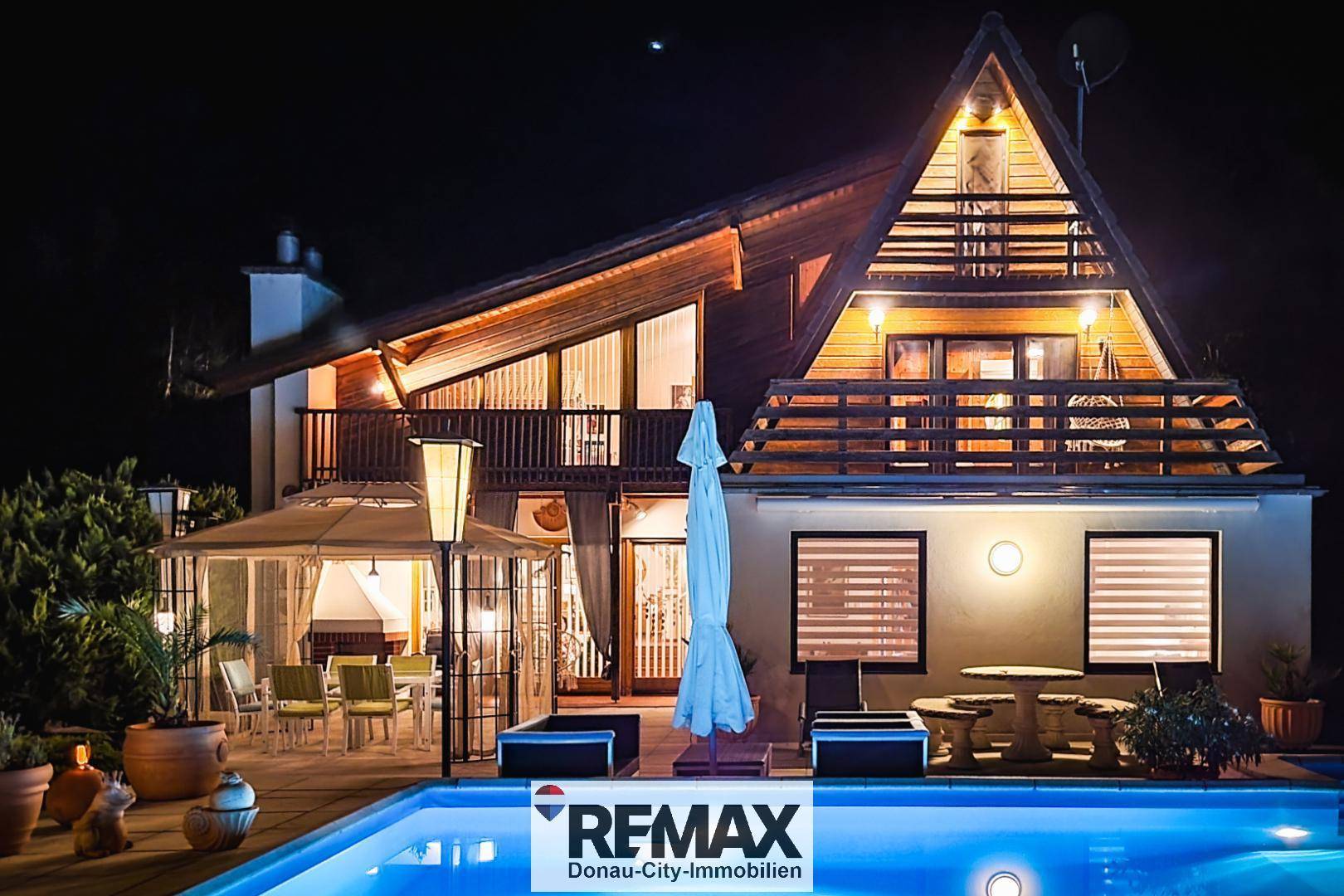 Beleuchtetes Holzhaus mit Poolbereich bei Nacht, mit reflektierendem Wasser und gemütlicher Atmosphäre.