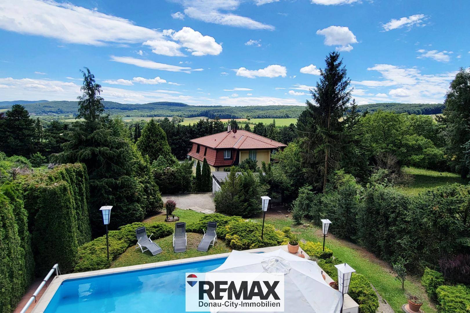 Weitläufiges Anwesen mit Pool und Fernblick über die grüne Landschaft unter blauem Himmel.