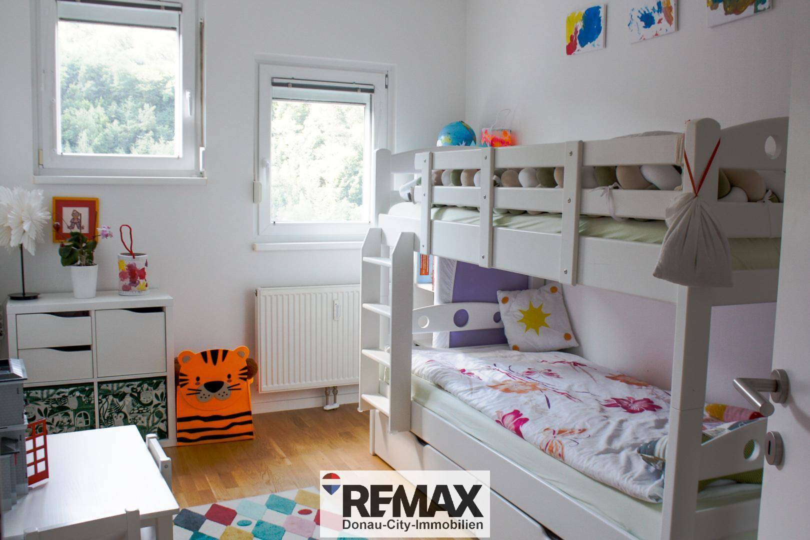 Helles Kinderzimmer mit Etagenbett, weißen Möbeln und farbenfroher Dekoration, ideal für Geschwister.