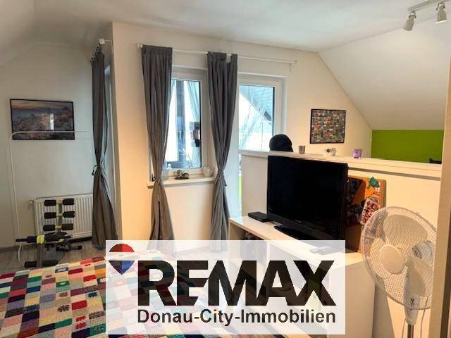 Helles Schlafzimmer mit Dachschrägen, Fernseher und Blick ins Grüne.