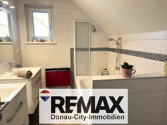Badezimmer im Dachgeschoss mit Badewanne, Fenster und Fliesen in Weiß und Grau.