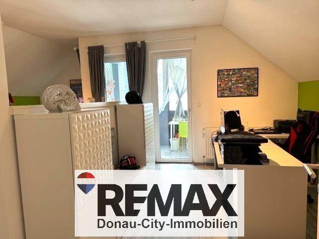 Schlafzimmer im Dachgeschoss mit Schrägen, Fenster und Zugang zu einem kleinen Balkon.