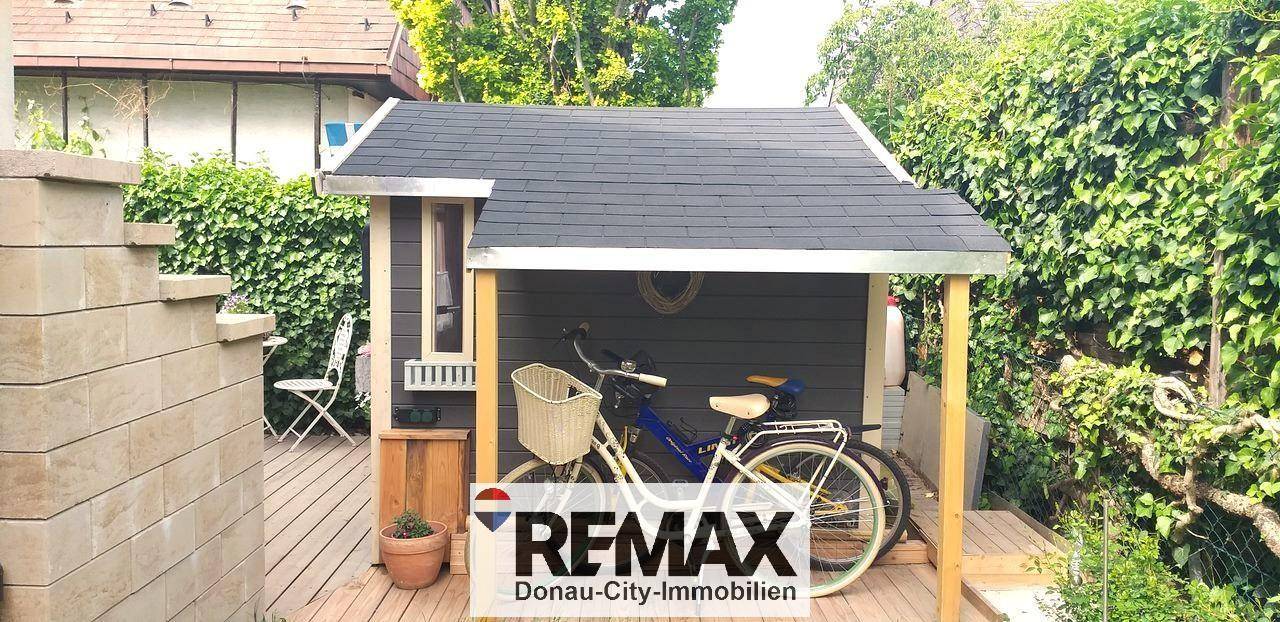 Kleines Gartenhaus mit Fahrradstellplatz und umgeben von grünen Hecken.