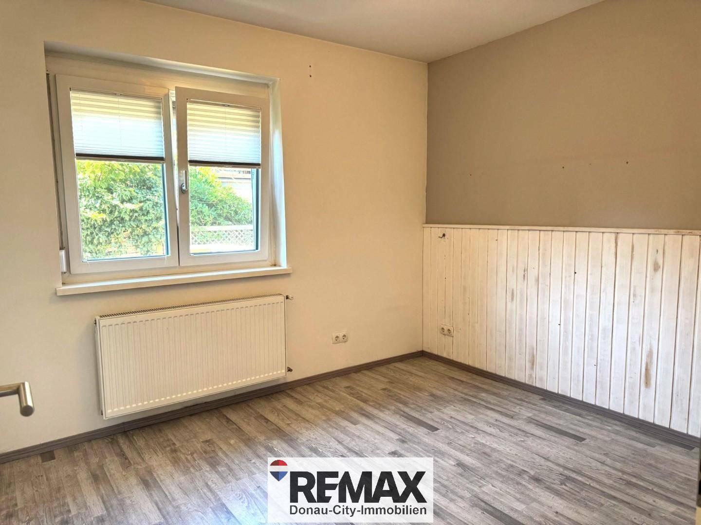 Schlafzimmer mit Holzboden, Fenster und teilweise holzvertäfelten Wänden.