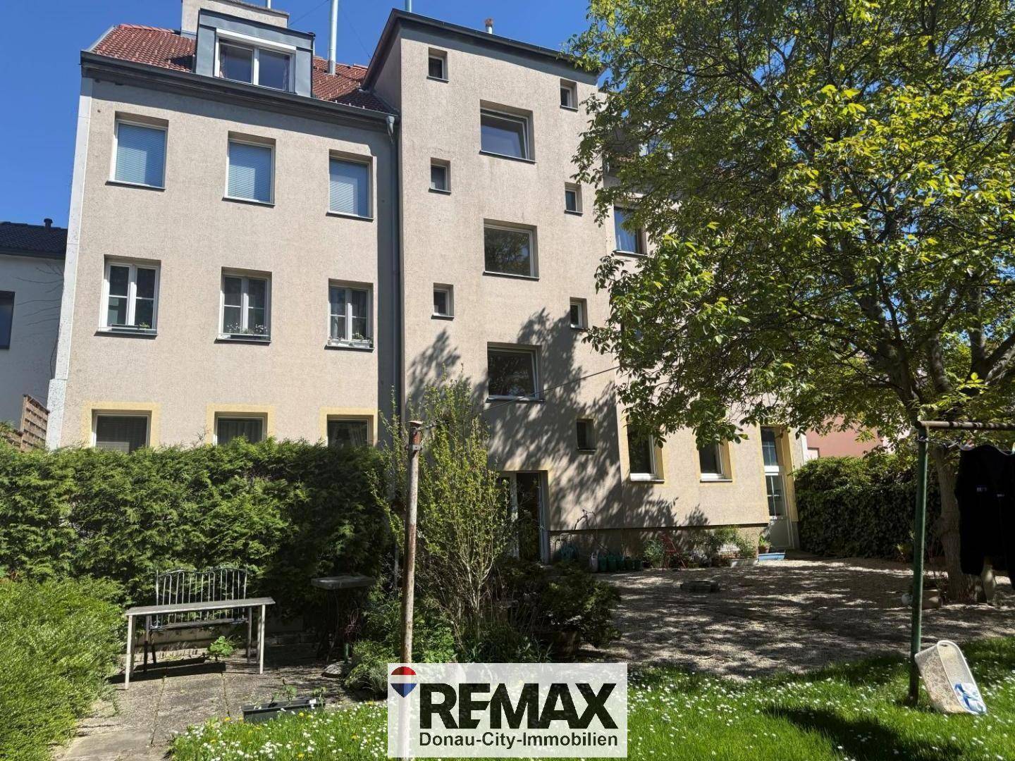 Mehrstöckiges Wohngebäude mit verschiedenen Fenstergrößen und Gartenbereich im Vordergrund.