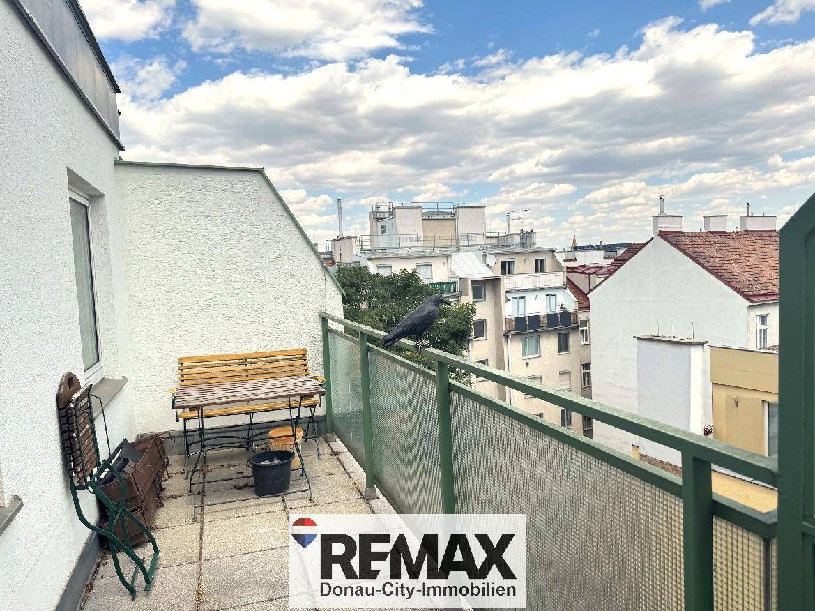 Balkon mit Sitzbank und Blick auf die umliegenden Gebäude der Stadt unter blauem Himmel.