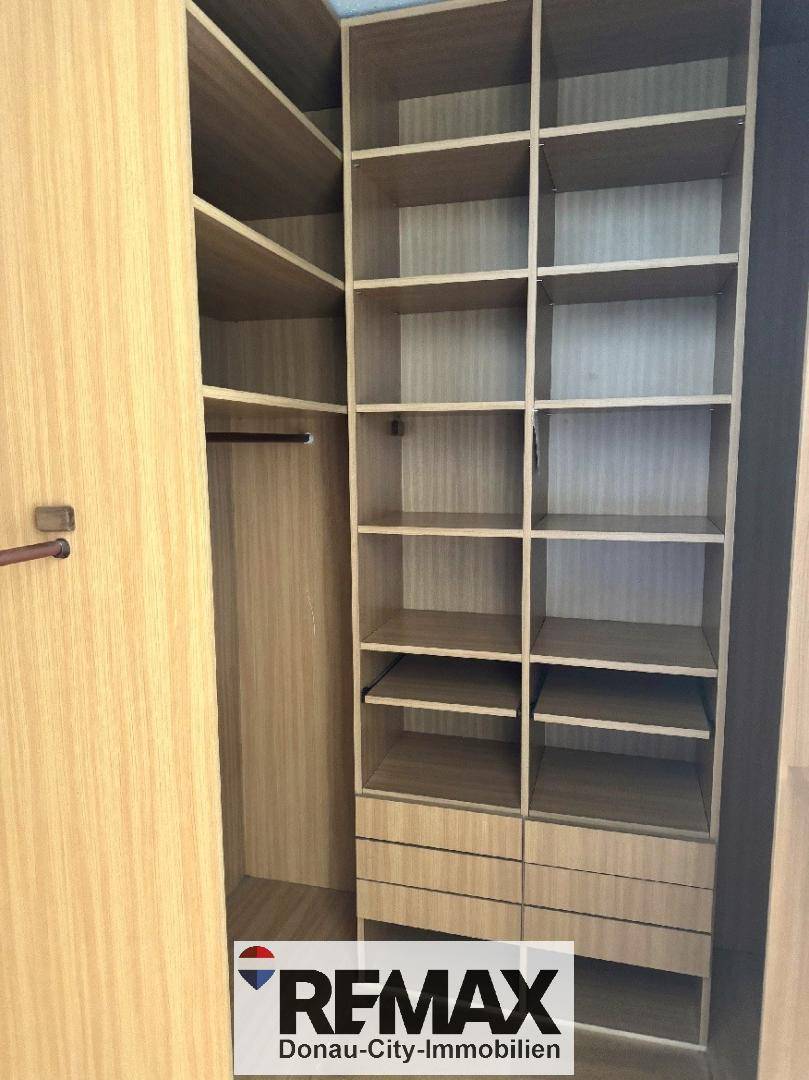 Geräumiger begehbarer Kleiderschrank mit vielen Regalen und Aufbewahrungsmöglichkeiten aus hellem Holz.