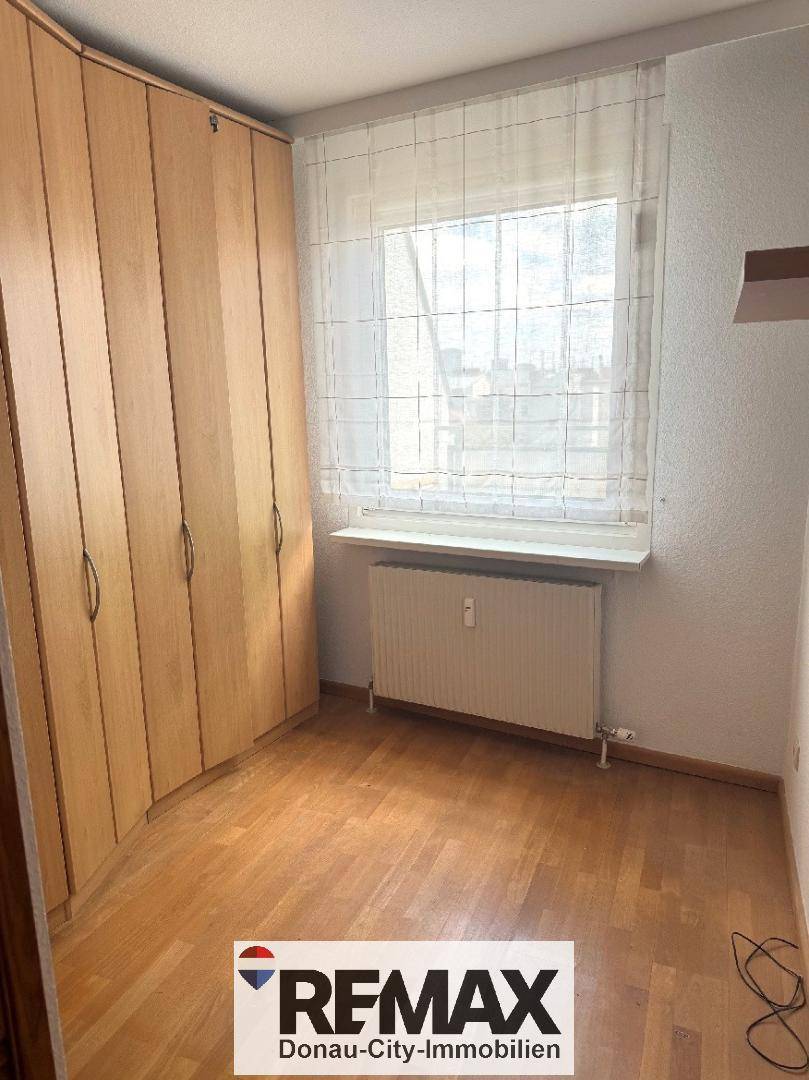 Schlafzimmer mit hellem Parkettboden und einem großen Einbauschrank, gut beleuchtet durch ein Fenster.