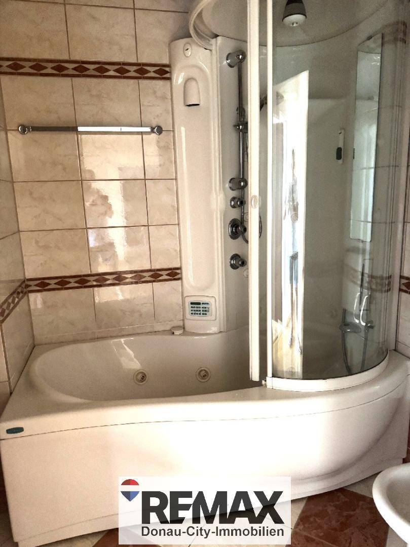 Badezimmer mit Eckbadewanne und integrierter Duschkabine, gefliest in hellen Farbtönen.