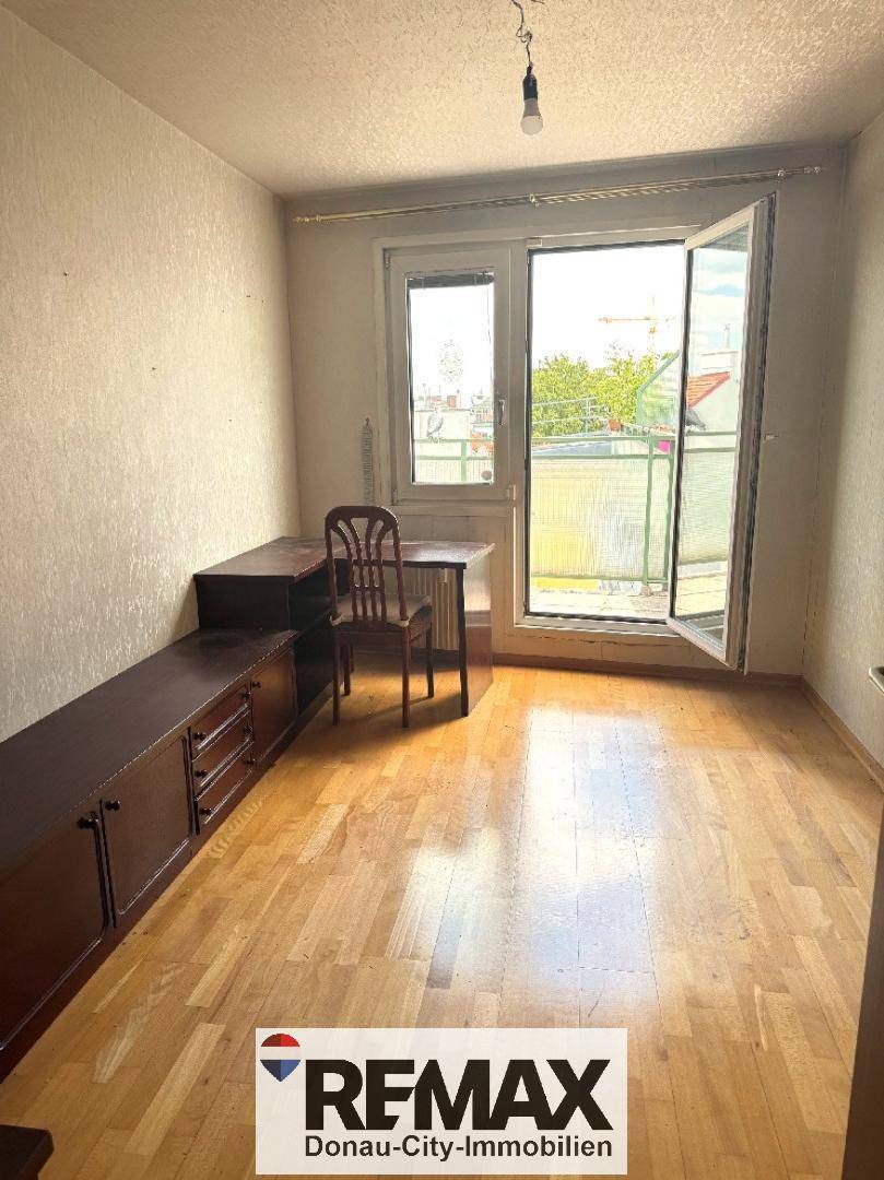 Helles Zimmer mit Parkettboden, einem Schreibtisch und Zugang zu einem kleinen Balkon.