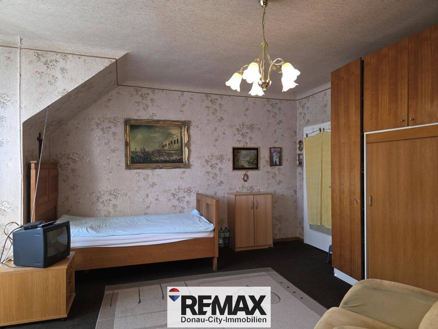 Schlafzimmer im Dachgeschoss mit Einzelbett, Schrank und gemusterter Tapete.
