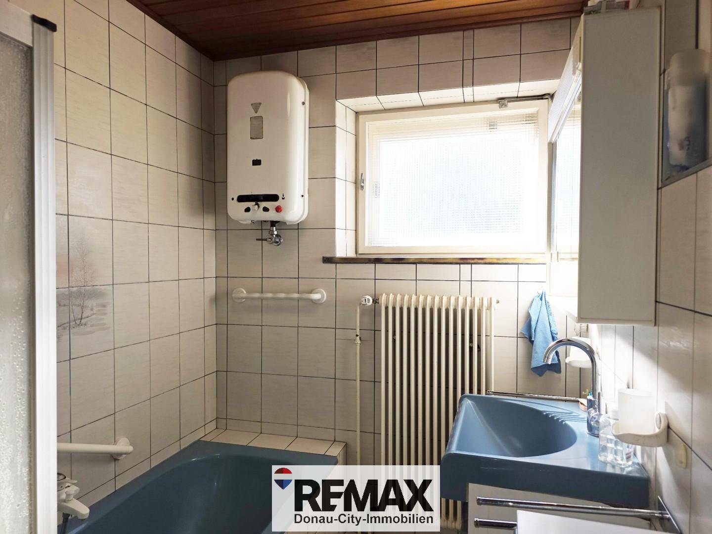 Badezimmer mit blauer Badewanne, Waschbecken und Fliesen, ausgestattet mit Haltegriffen.
