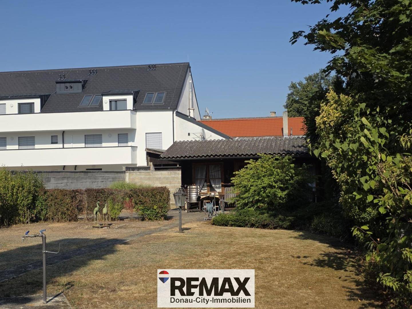 Gepflegter Garten mit Rasenfläche und überdachtem Sitzbereich im Hintergrund.