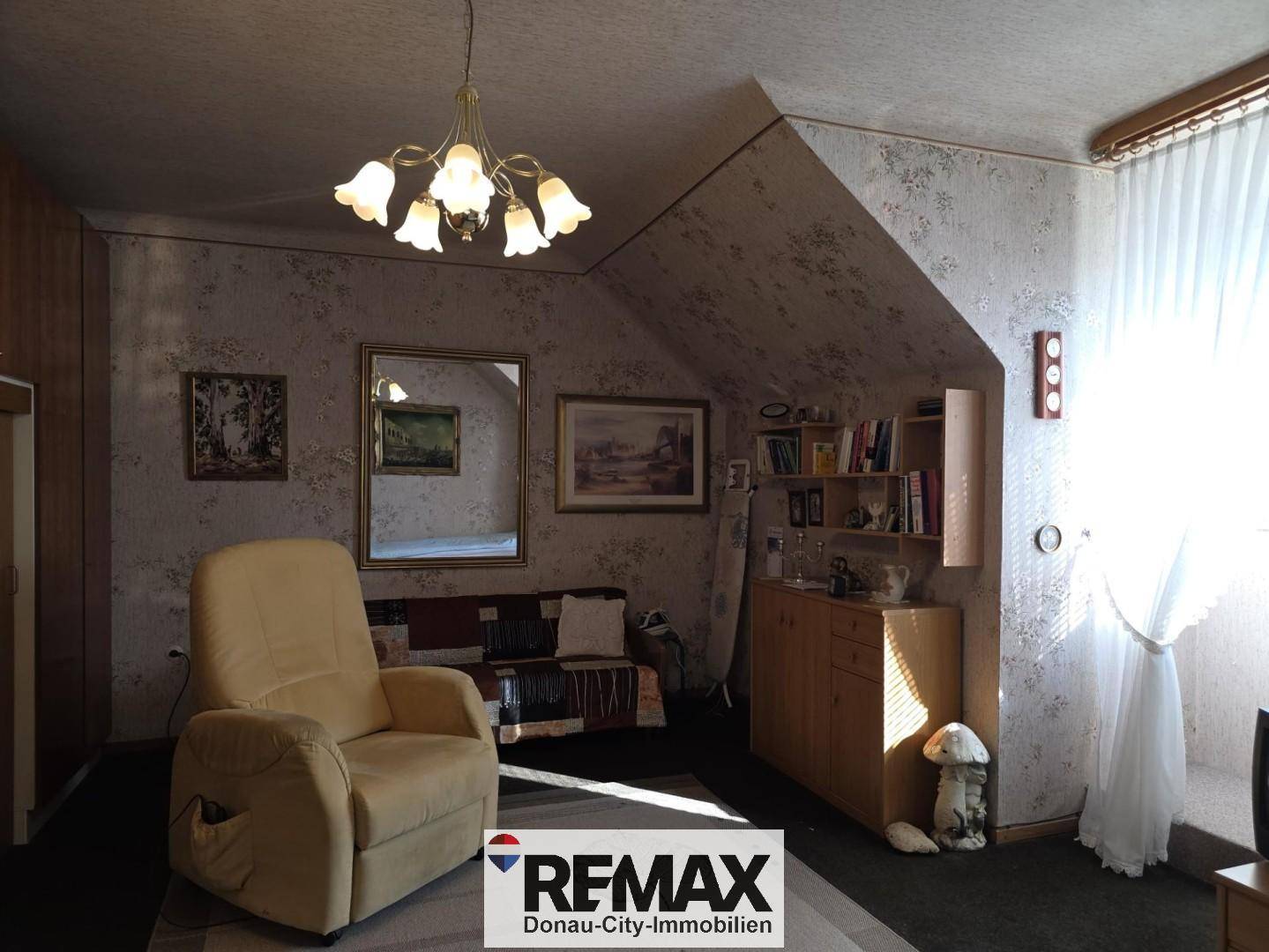 Schlafzimmer im Dachgeschoss mit schrägen Wänden, gemusterter Tapete und Sessel.