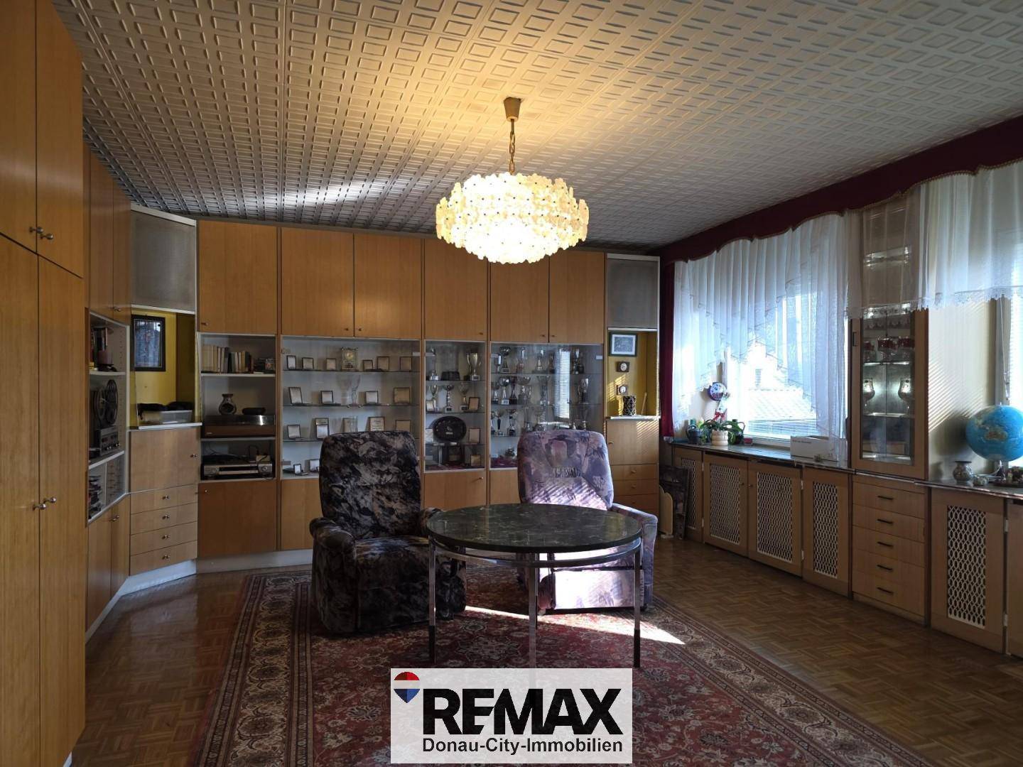 Geräumiges Wohnzimmer im Vintage-Stil mit Holzmöbeln, gemusterter Decke und Kronleuchter.