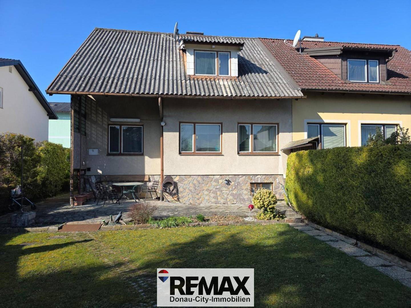 Rückseite des Hauses mit kleiner Terrasse, Gartenmöbeln und grünem Rasen.