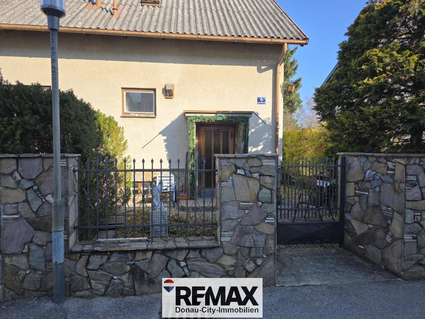 Vorderansicht eines Hauses mit Steinfassade und schmiedeeisernem Zaun.