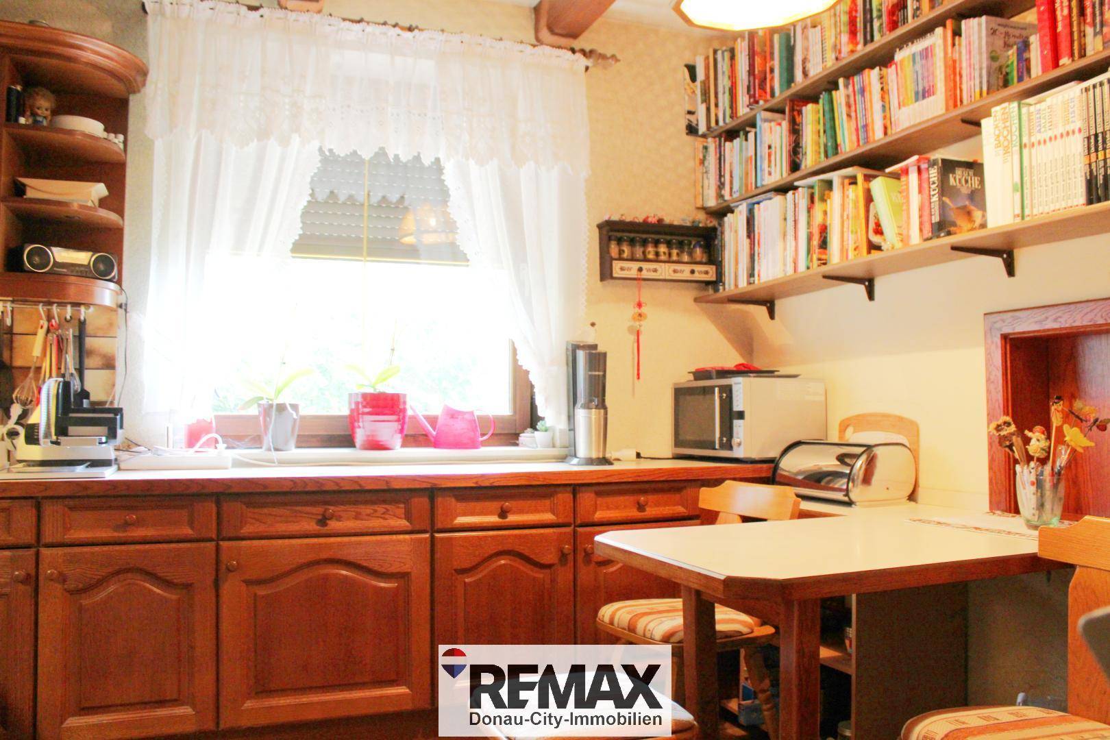 Traditionelle Küche mit Holzschränken, Fenster und integrierten Regalen für Kochbücher.