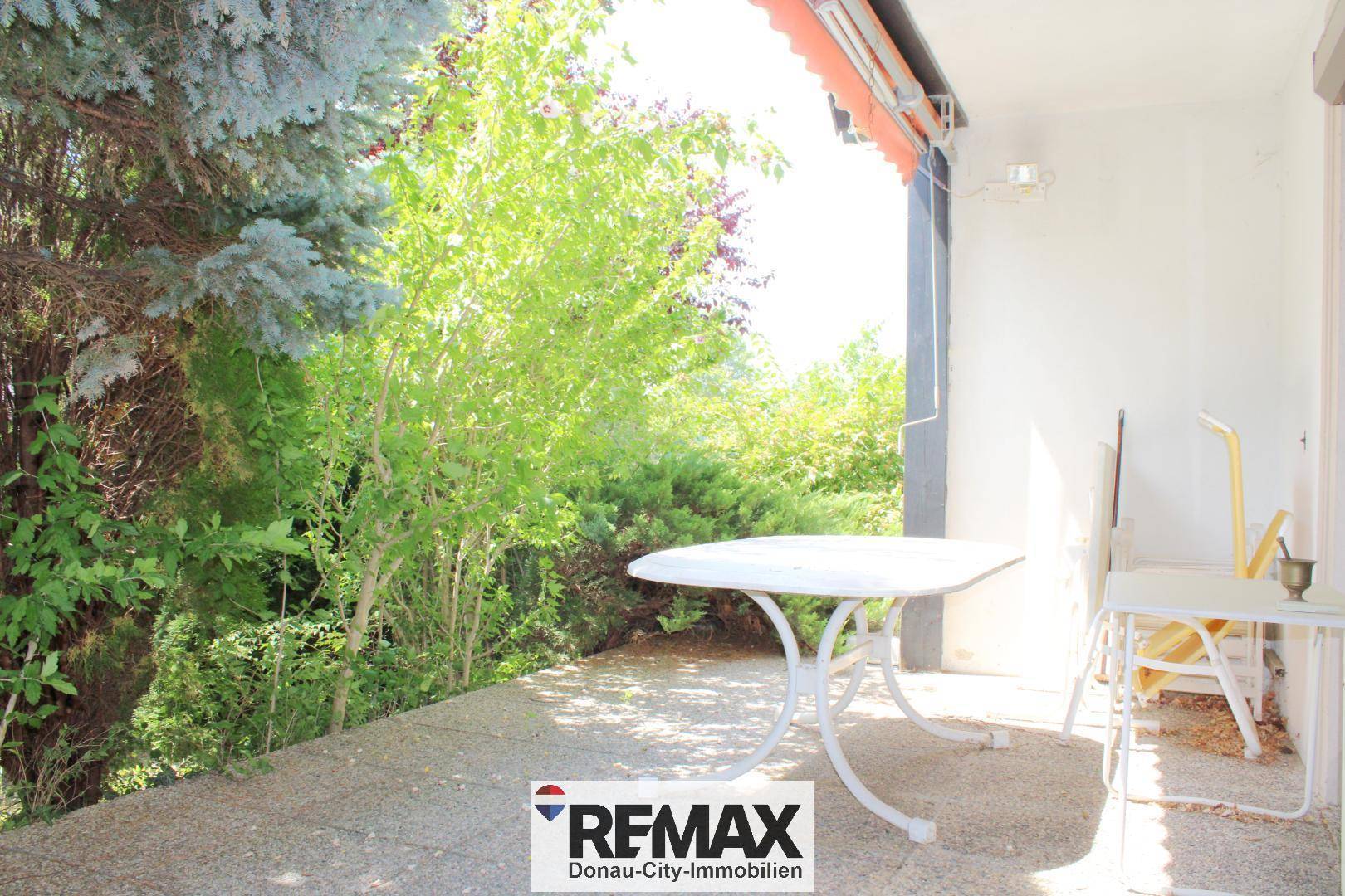 Sonniger Terrassenbereich mit Gartentisch und Stühlen, umgeben von üppigem Grün.