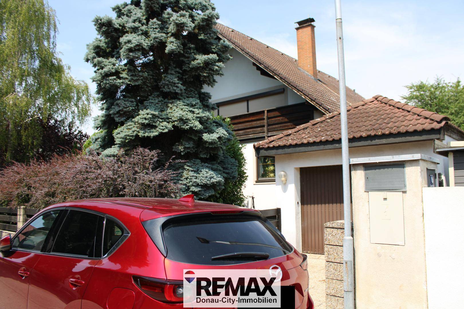 Seitenansicht des Hauses mit Garage und einem geparkten roten Auto auf der Einfahrt.