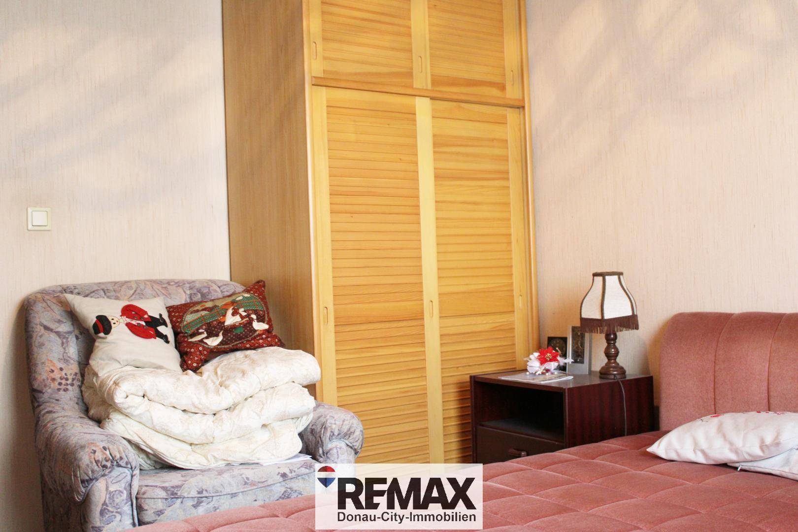 Schlafzimmer mit Einzelbett, Nachttisch und einem großen Holzschrank mit Lamellentüren.
