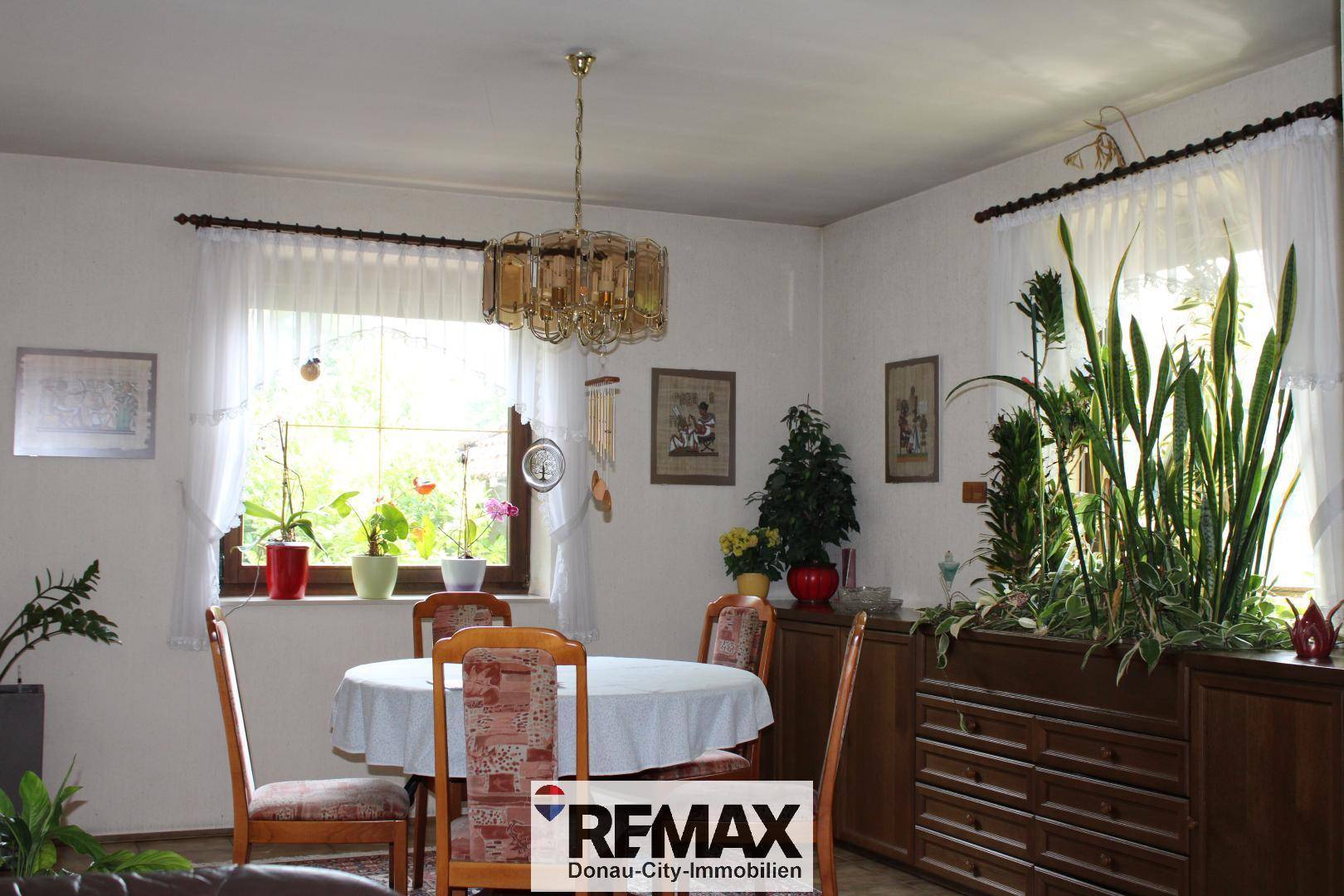 Heller Essbereich mit großem Fenster, Esstisch und vielen Pflanzen, die eine freundliche Atmosphäre schaffen.