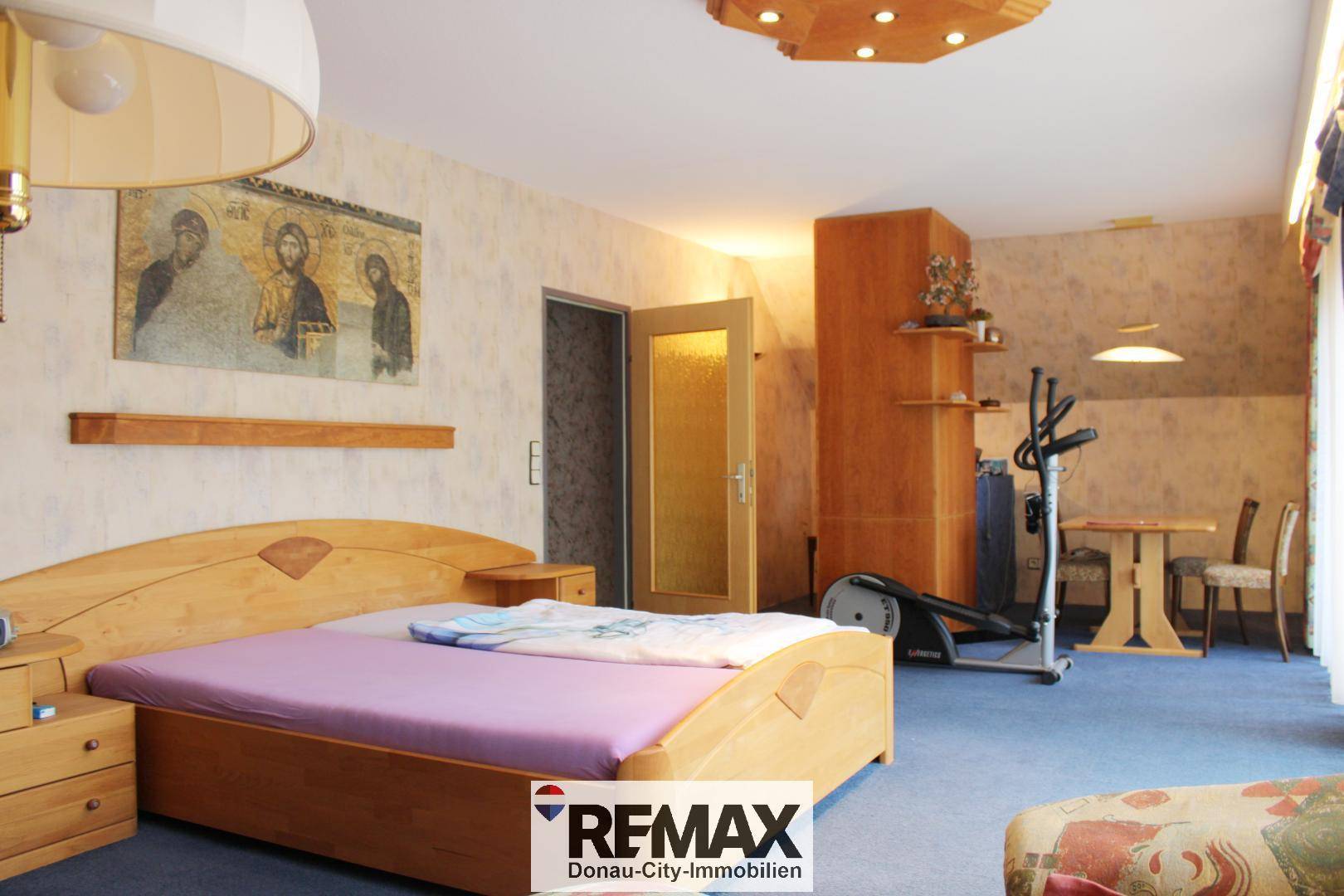 Schlafzimmer im Dachgeschoss mit Doppelbett, Fitnessgerät und Zugang zu einem weiteren Raum.